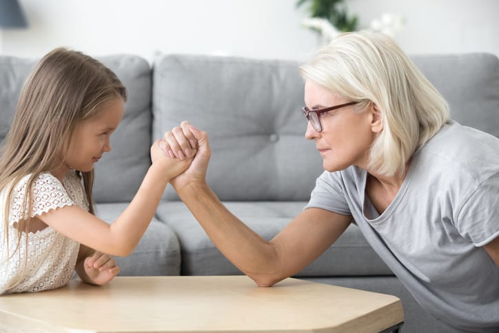 Old grandma and little granddaughter arm wrestling playing together