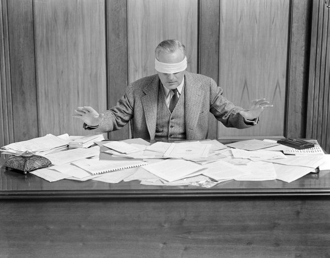 Blindfolded Businessman At Desk Covered With Papers.