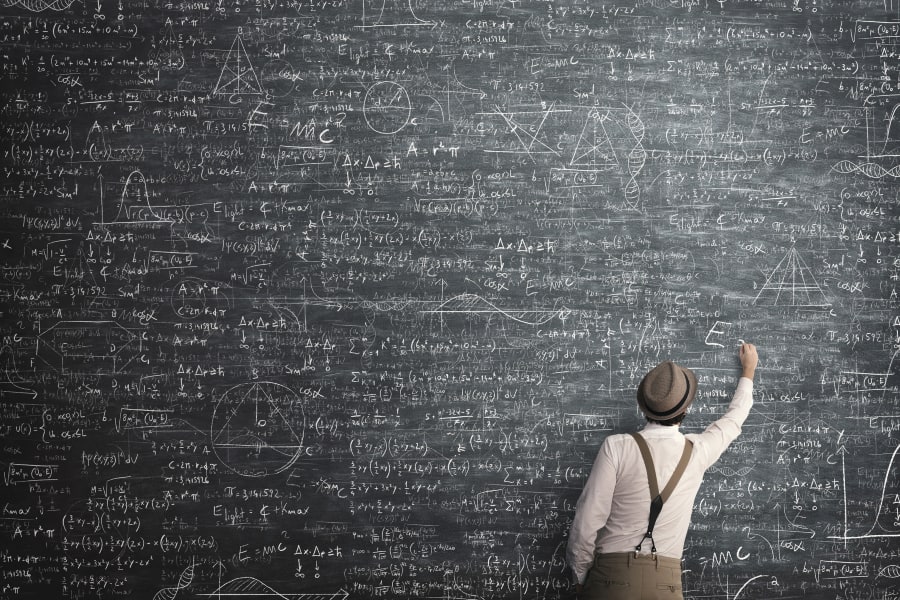 Man with hat writing challenging formulas on chalkboard