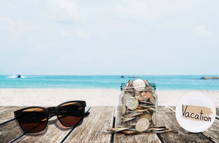 Saving money for vacation concept, glass coins container with sunglasses
