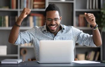 Happy african guy looking at laptop screen, cheering