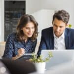 Two business people sitting at cafe working on new project using laptop. Young businesswoman taking notes and businessman working on laptop computer.