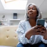 Mature black woman at home texting on her cell phone while sitting on the couch