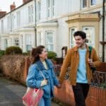 Front view of a young couple walking down terraced Street in Whitley Bay in the north-east of England they are heading into the town centre and deciding which shops to go to they are also holding hands and carrying bags over their shoulders.