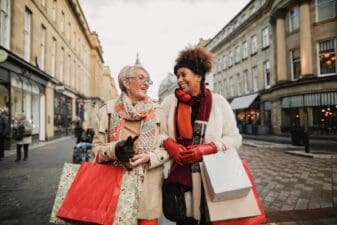 Two female adult friends walking through the city streets at Christmas. They are talking and smiling as they do some Christmas shopping.