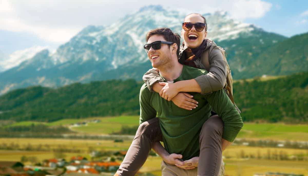 travel, tourism and people concept - happy couple with backpacks having fun over alps mountains background