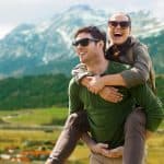 travel, tourism and people concept - happy couple with backpacks having fun over alps mountains background