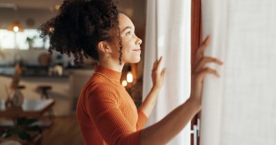 Curtains, happy woman and thinking of future in home, planning and reflection of mindset with view. Window, smile and African girl with vision, ideas and dream for morning inspiration in living room.